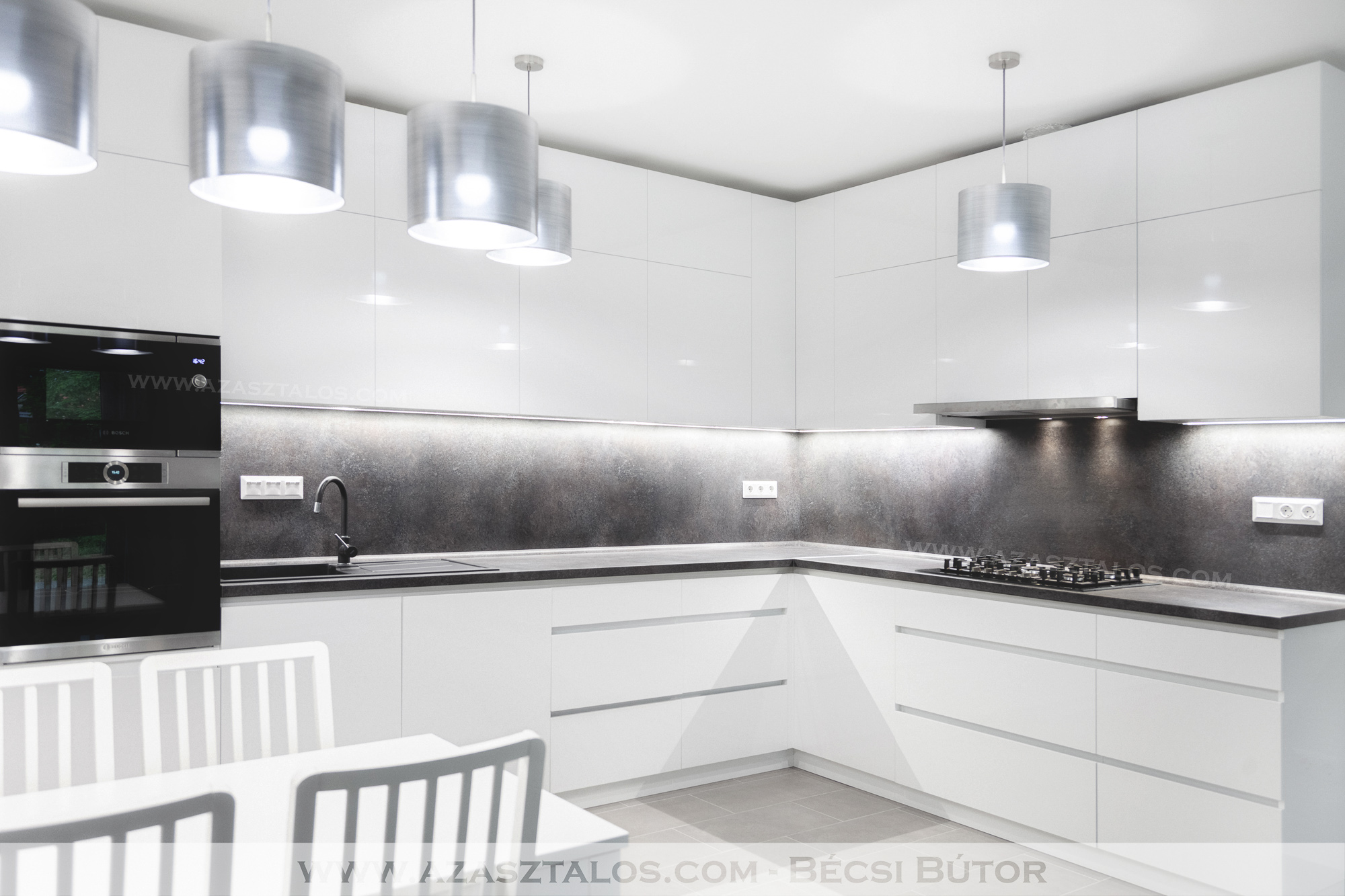 A konyha különleges szépségét a magasfényű fehér Rehau Rauvisio brilliant ajtófrontok és az Egger hátpanel összhangja adja leginkább. A konyhabútor további különlegessége, hogy a munkalap, a hátpanel és a vízzáró színe megegyezik, így mintha egy anyagból készült volna az egész. FDS slim csillapított behúzású fiókok, Titus t-type csillapított záródású kivetőpánt került felhasználásra. A pántot gyors csukódás és rövid csillapítási út jellemzi, a több százezer csukódást kibíró élettartama mellett, valamint a csillapítás mértéke a megrendelő igényei szerint állítható. A gyárilag tiszta alumínium színű Gola fogantyú profil fehér színterezést kapott. A felsőrész aljára extra fényerejű LED szalag került. Végül, de nem utolsósorban egy Kesseböhmer LeMans II sarokvasalat is helyet kapott a sarokban.